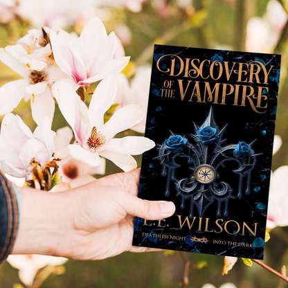 Hand holding a book titled 'Discovery of the Vampire' by L.E. Wilson with flowers in the background